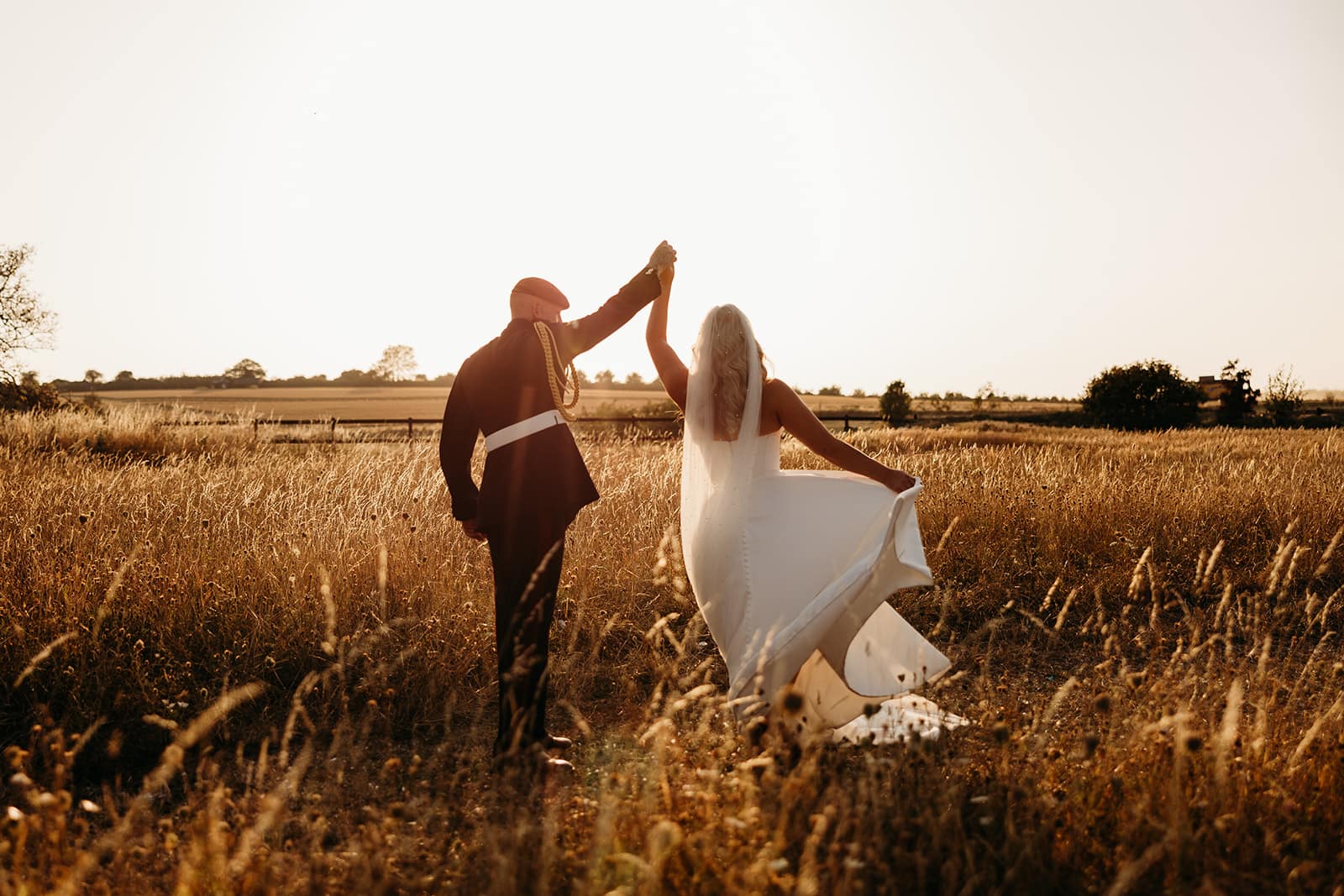 A couple walking into the low sun across the long grass, her train catching the light