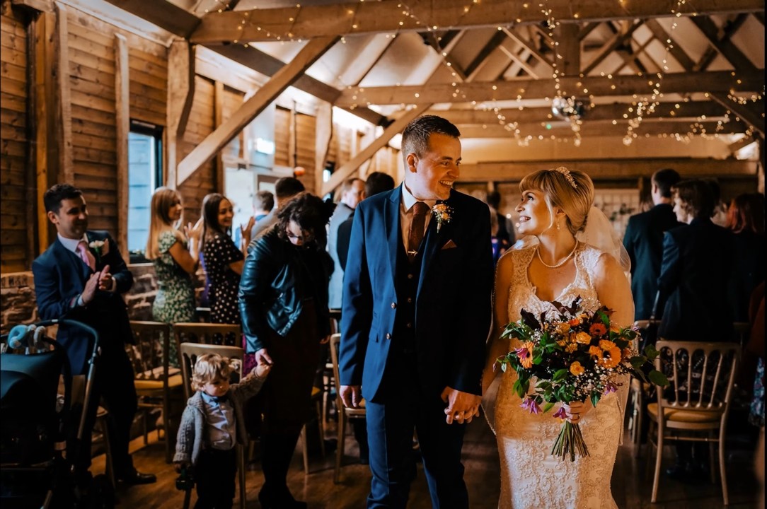 A couple walking back down the aisle, guests either side under fairy lights