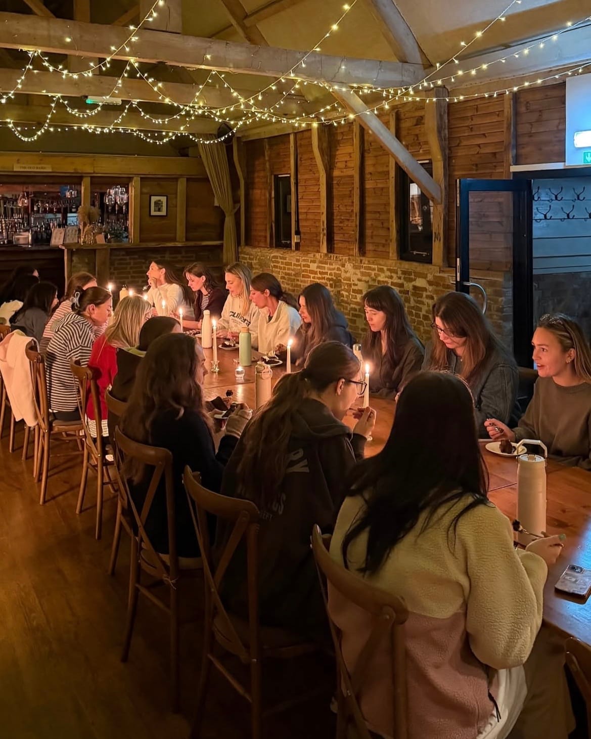 The group at a long candlelit table in the barn under strings of lights
